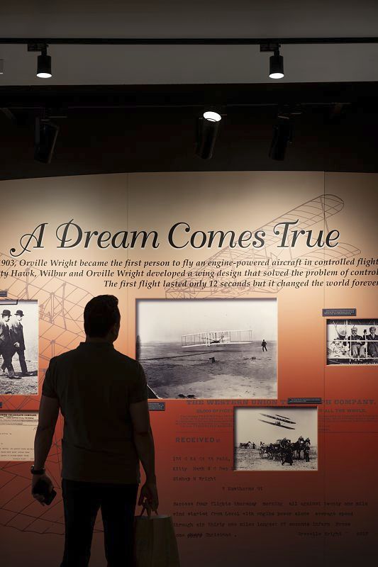 Visitor views exhibit on flight pioneers at Cradle of Aviation Museum, lit by ERCO LED spotlights.