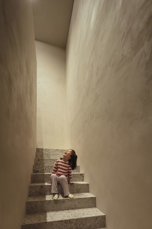 Girl sits on stairs in Daisy Home, illuminated by ERCO lighting for a comfortable ambiance.