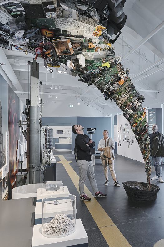 Visitors view e-waste sculpture at Deutsches Museum, illuminated by ERCO LED spotlights.