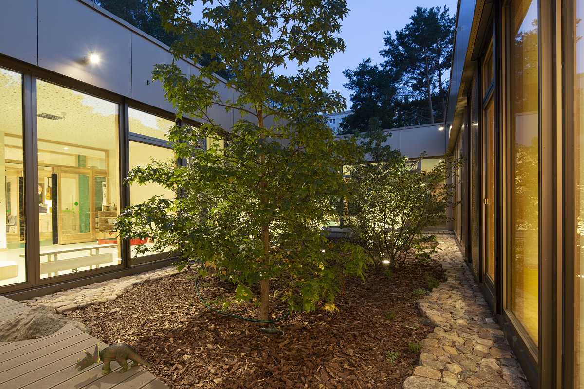 Illuminated outdoor area of Rappelkiste Day Care Centre with trees and ERCO lighting for visual comfort.
