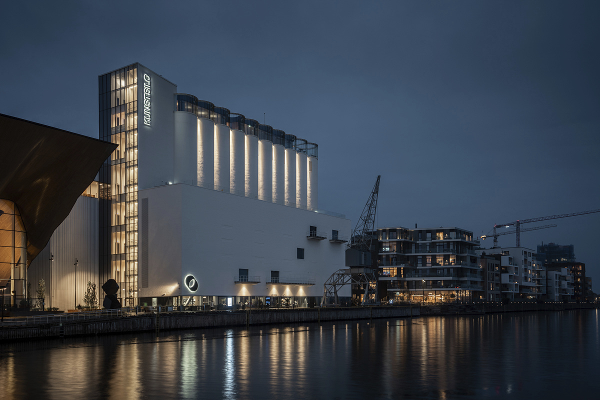 Kunstsilo Kristiansand art museum, illuminated at dusk, reflecting in the waterfront.