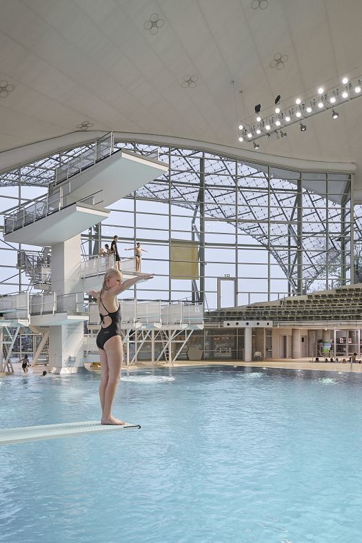 Diver on springboard at Munichs Aquatic Centre, lit by ERCO LEDs for energy efficiency and visual comfort.
