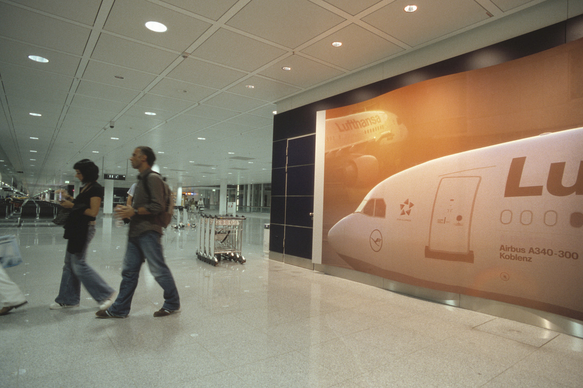Airport terminal featuring a Lufthansa plane ad and passengers under ERCO Lightcast LED lighting.