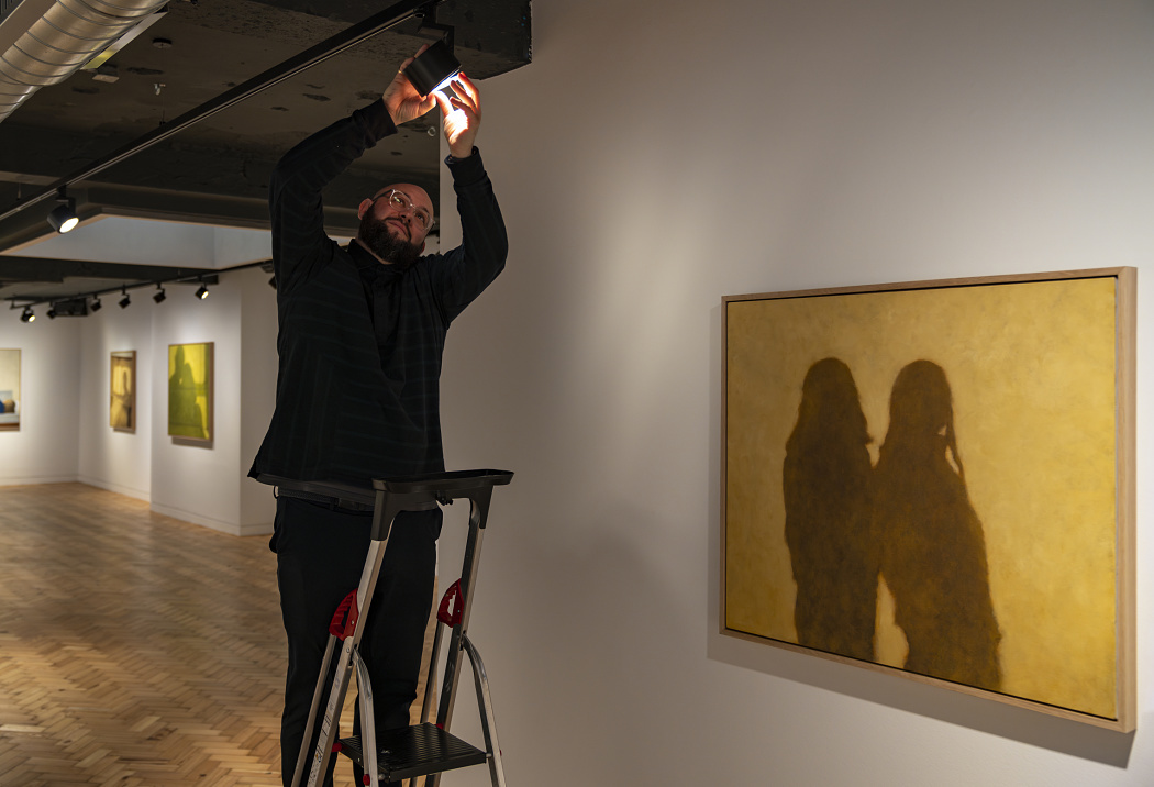 Gallery staff adjusts an ERCO spotlight on a ladder to optimally illuminate an artwork.