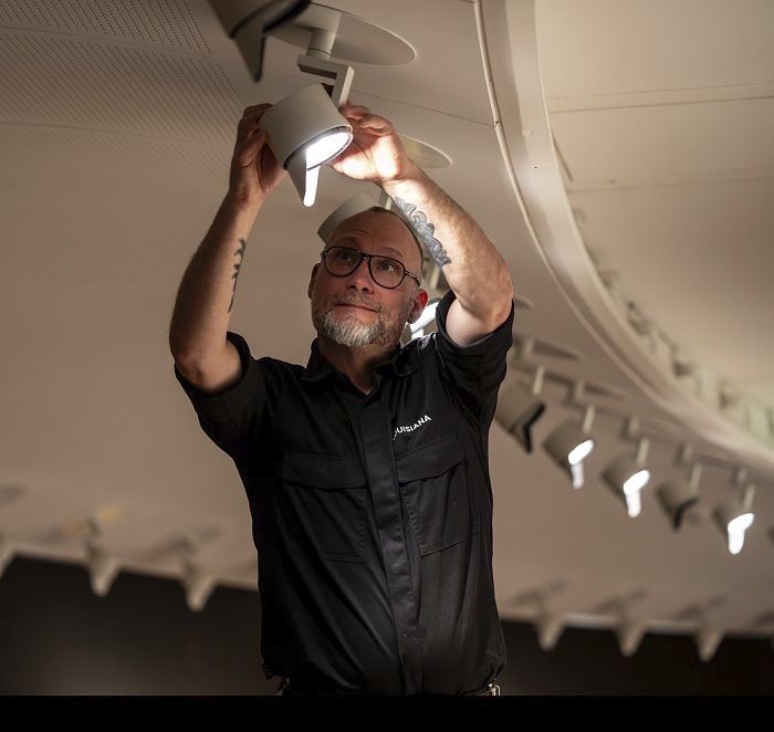 A man adjusts an ERCO spotlight in a gallery, optimizing the lighting for the artwork.