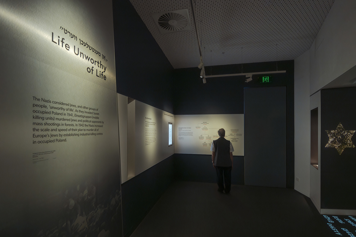 Visitor in Melbourne Holocaust Museum, illuminated by ERCO spotlights accentuating exhibits.