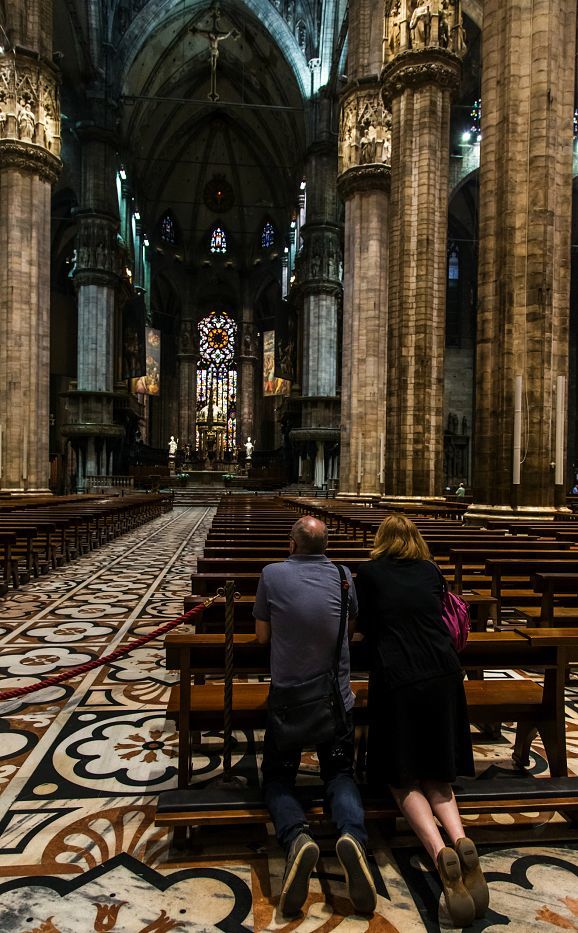Interior of Milan Cathedral featuring LED lighting and people in prayer.