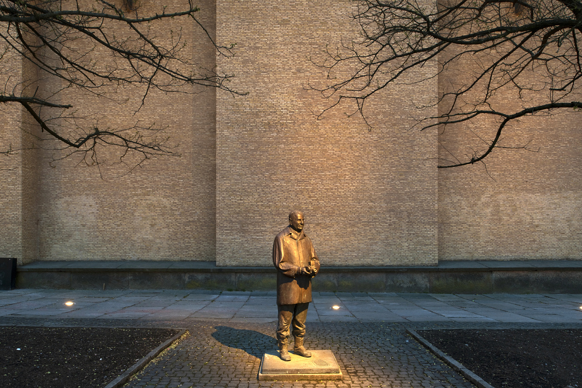 Illuminated statue in front of brick wall, museum outdoor area with ERCO lighting.