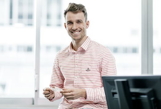 ERCO employee: Man smiles, holding clear aligners in the office.