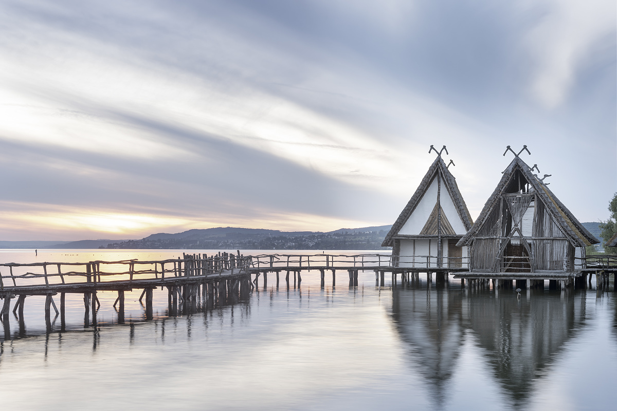 Pfahlbaumuseum Unteruhldingens stilt houses on Lake Constance, illuminated at sunset.